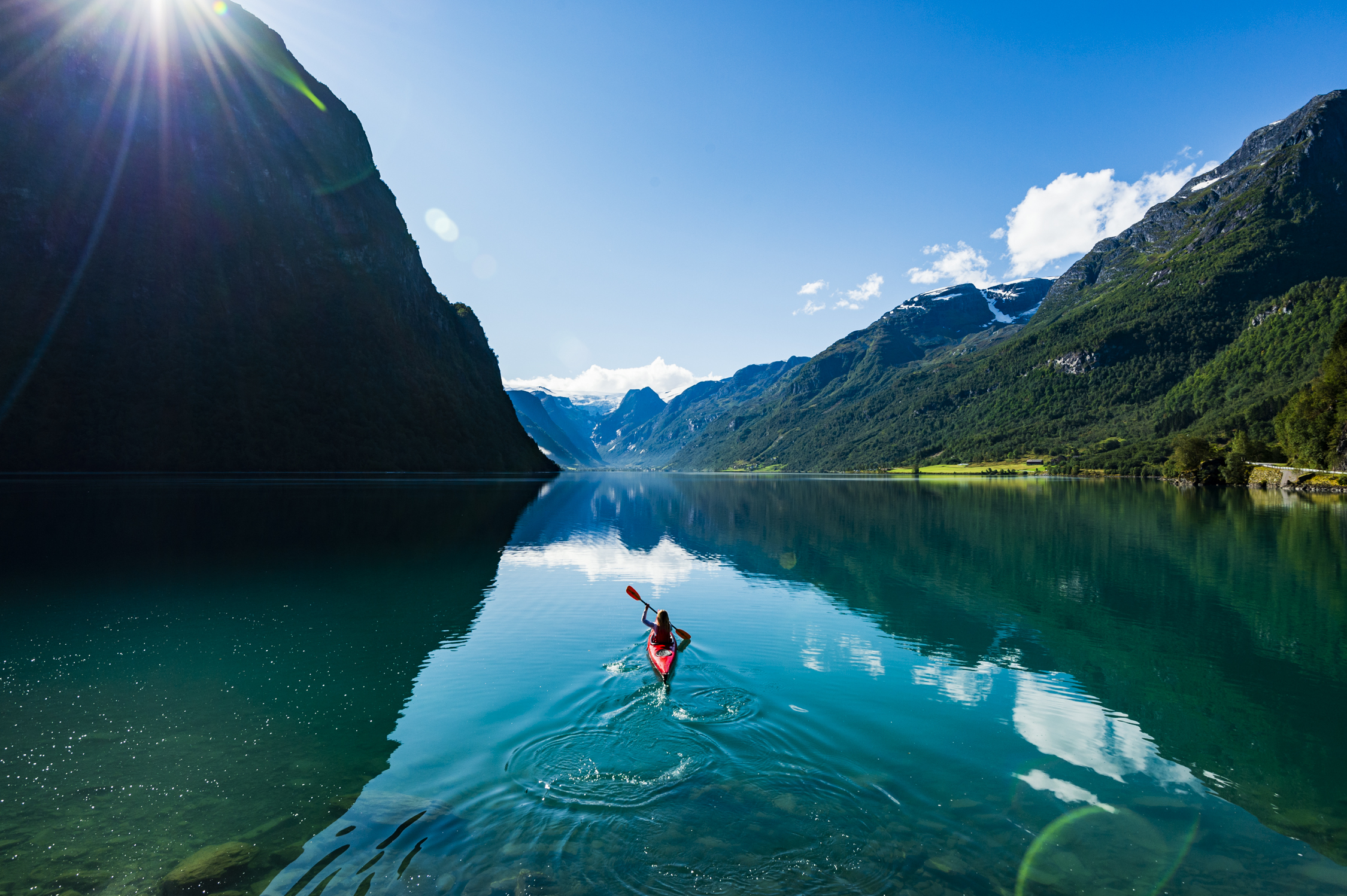 Foto av kvinne som padler i rød kajakk i stille vann, Oldevatnet i Stryn